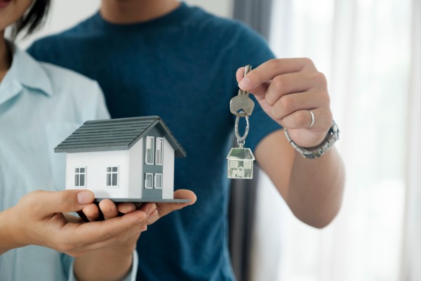 Person holding model of house while another person holds a pair of keys